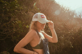 A woman paddle boarding on a lake wearing a Voltage Trucker hat