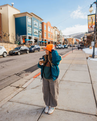 Annie Hernandez Standing on the sidewalk drinking coffee wearing an orange Voltage beanie