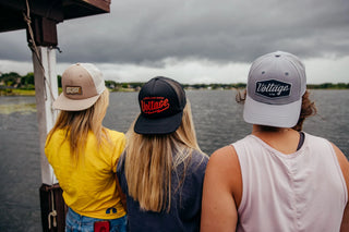 3 Women looking out on a big cloudy lake wearing voltage hats backwards