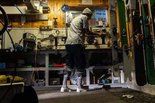 A man waxing his skis in a warehouse with voltage snow socks on