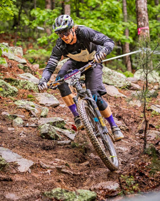 an athlete mountain biking in a rocky forest wearing purple voltage socks