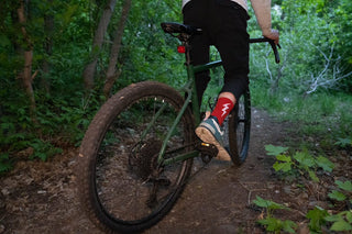 Man riding a bike in a dense, dark forest wearing red lucky socks