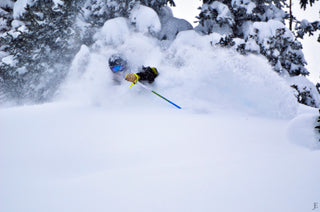 Skiier cutting into the snow and skiing through a cloud of powder