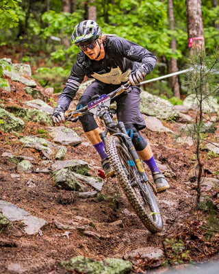 Man mountain biking in purple KOM socks in a mossy forest