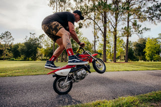 Man standing on a small motor bike doing a wheelie wearing red lucky socks